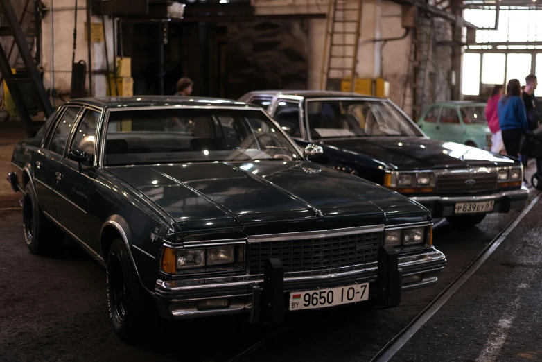 three cars parked in a garage with a few pedestrians