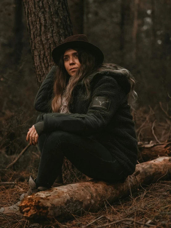 a man wearing a hat sitting on a log in the woods