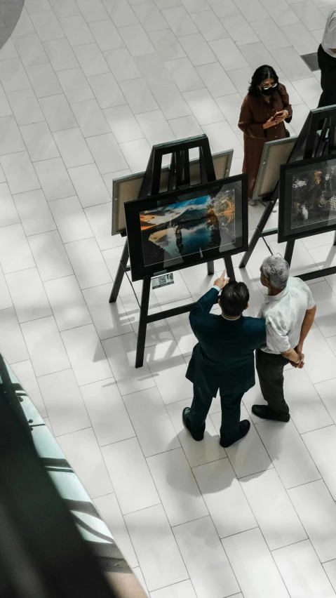 three people are standing around two easels and looking at paintings