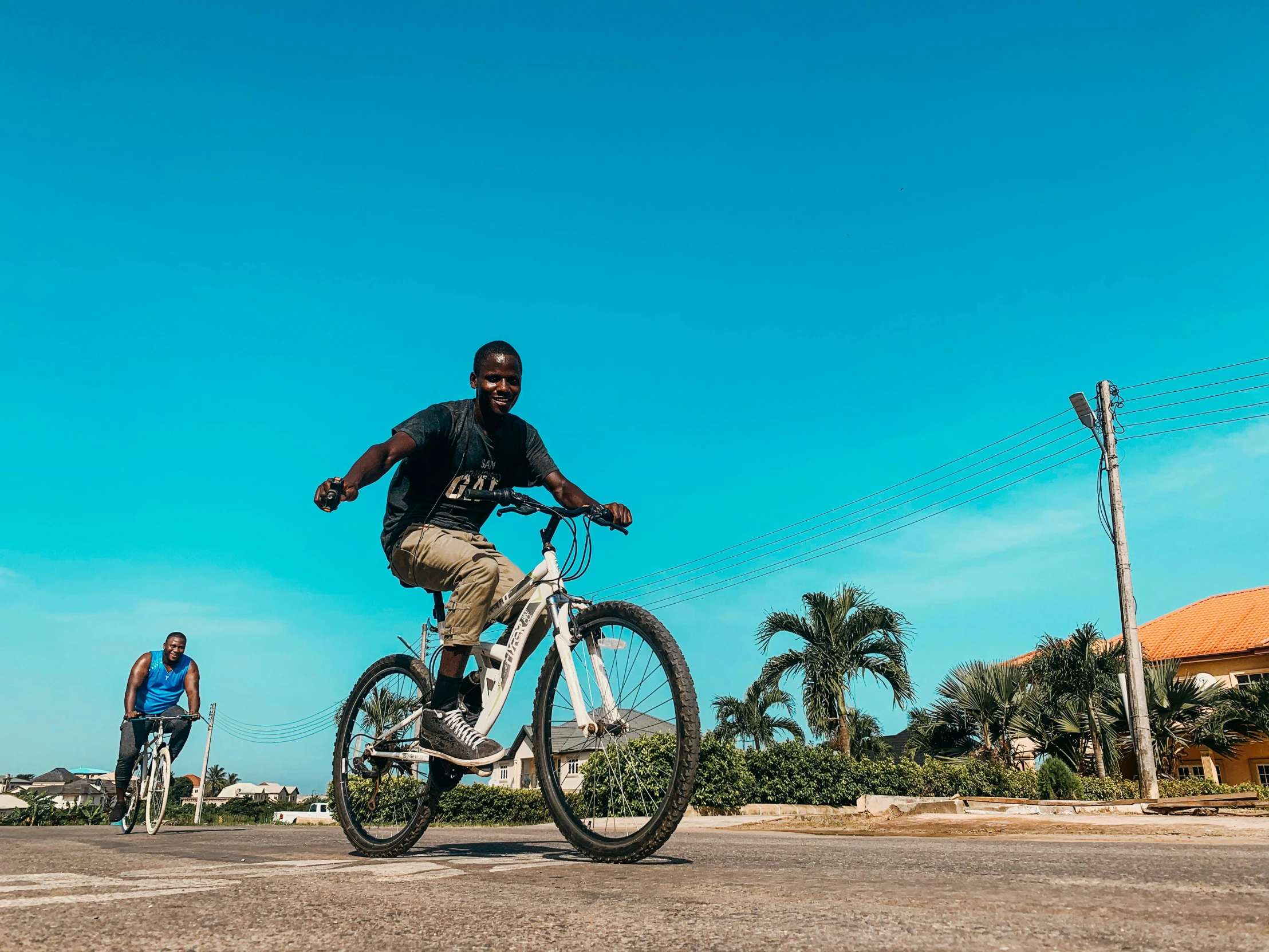 two people riding bicycles on a street with palm trees