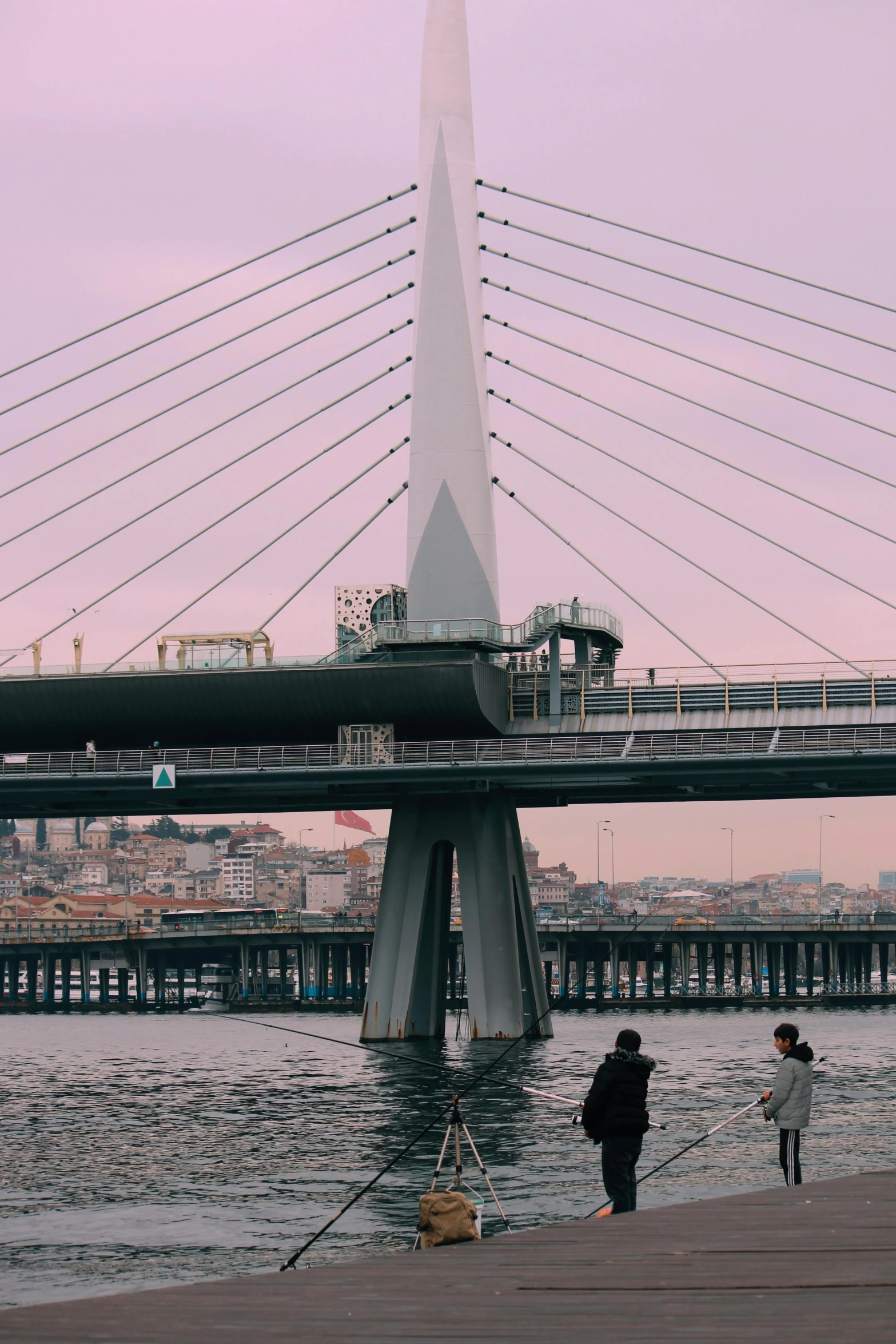 people walking on the shore of a lake in front of a bridge