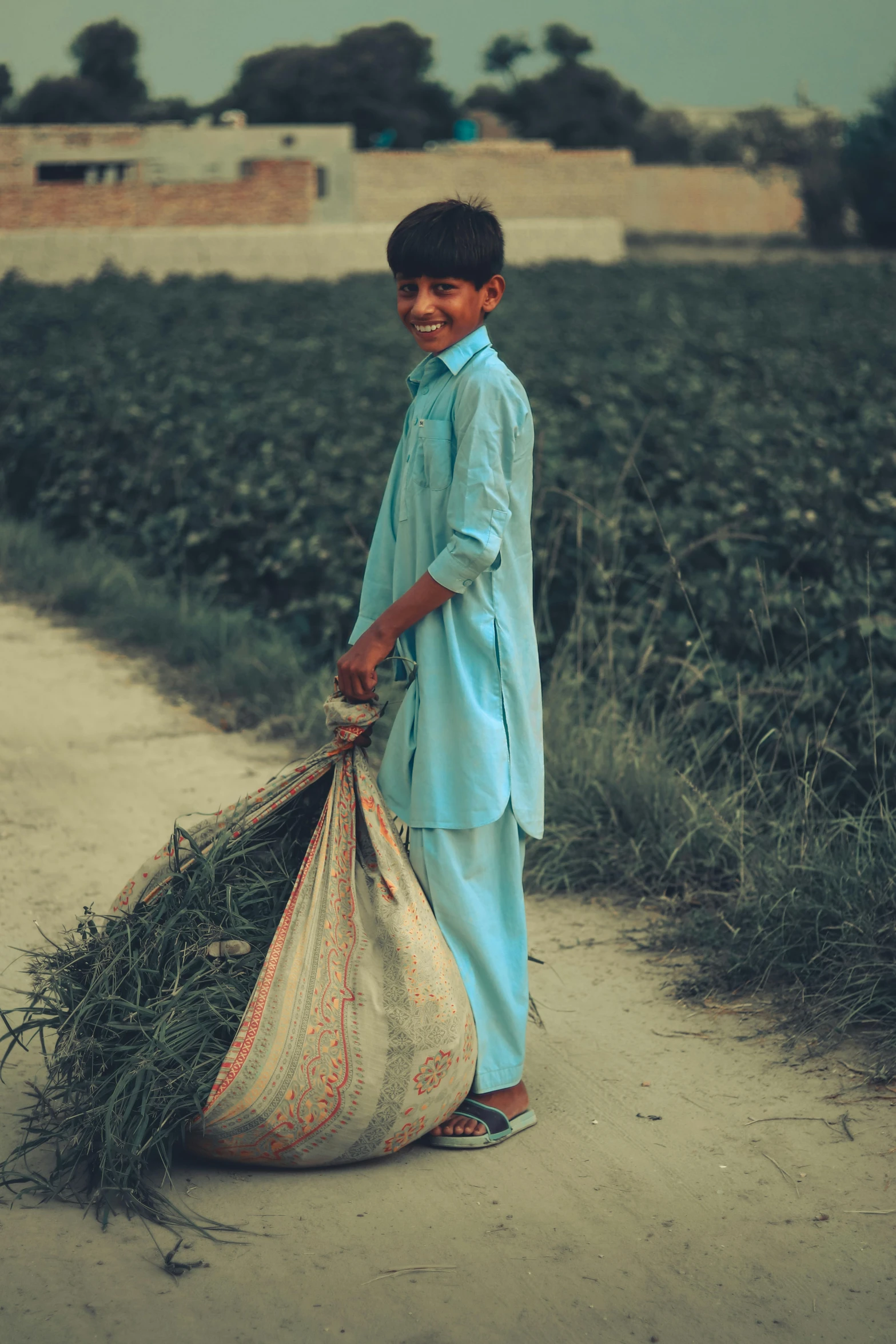 the boy stands beside the field with his bag