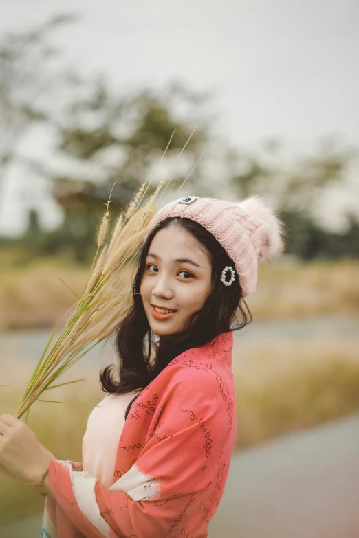 an asian girl in pink jacket holding grass with hat