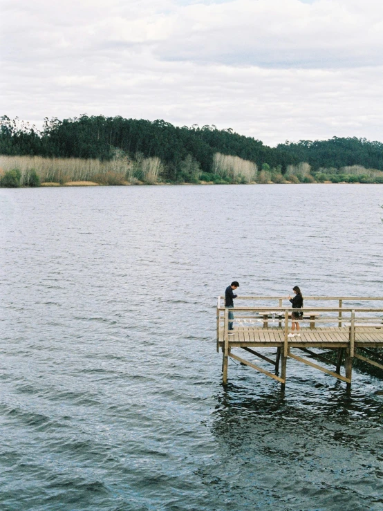 two people are sitting on the pier near a body of water