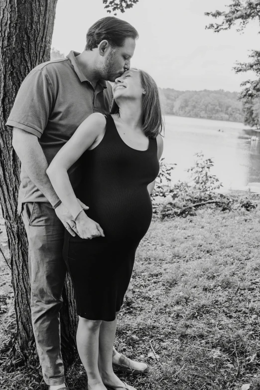 an expective pregnant couple leans against a tree for their portrait