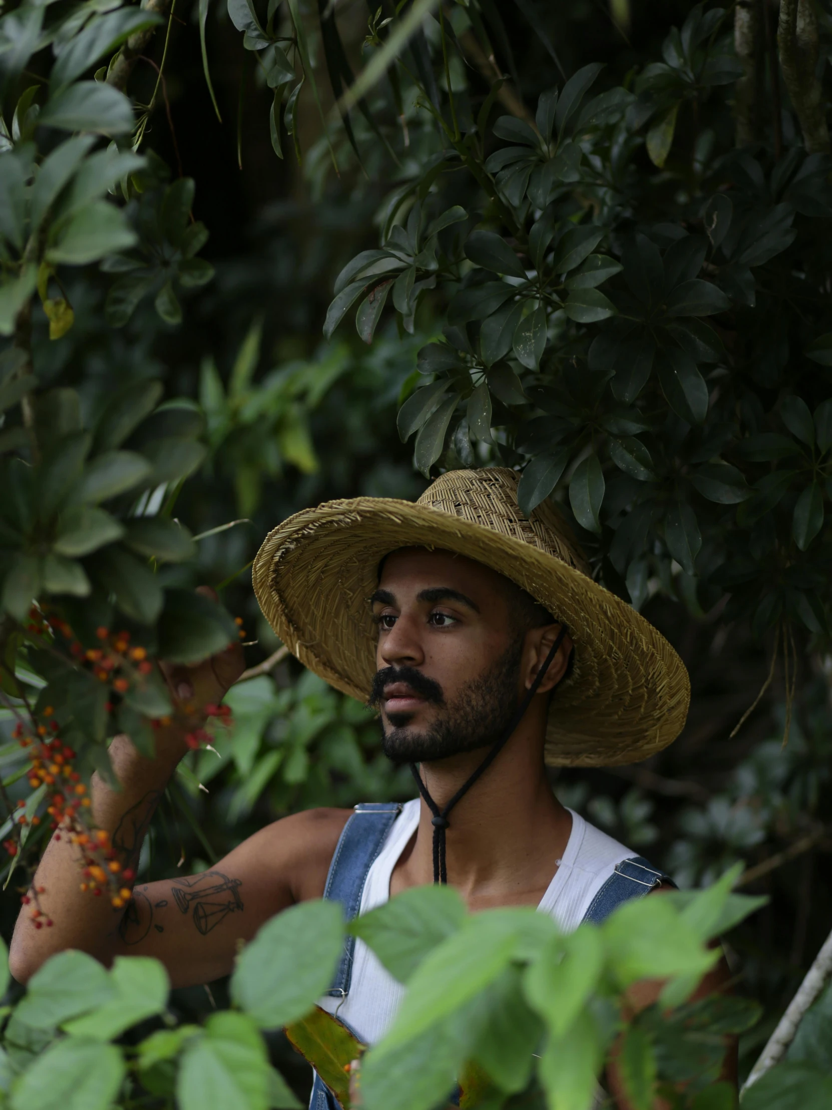 a man wearing a hat, a vest and an apron standing next to a tree