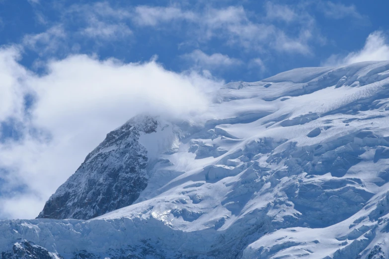 mountains covered in snow under a blue cloudy sky