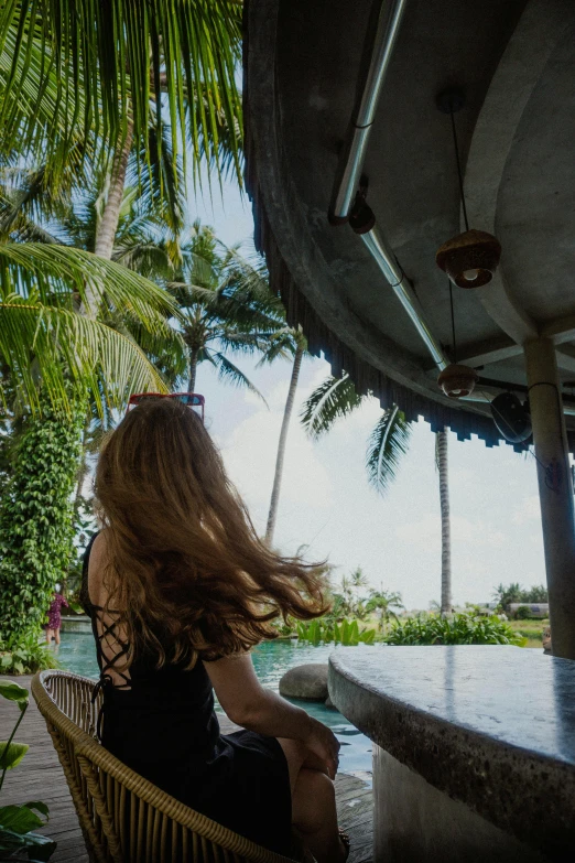 a woman in a black dress sits on a chair near the water