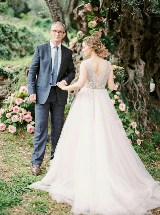 a couple hold hands in front of a wedding arch and rose bush