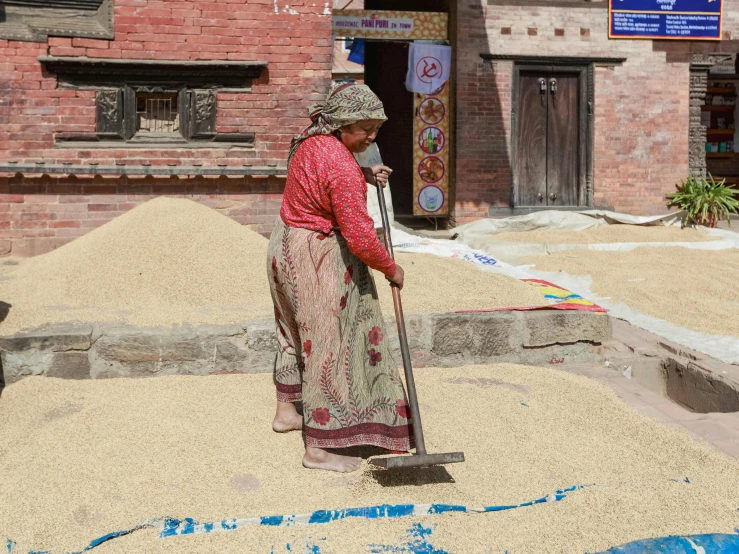 a lady in a pink and grey dress cleaning a pile of sand