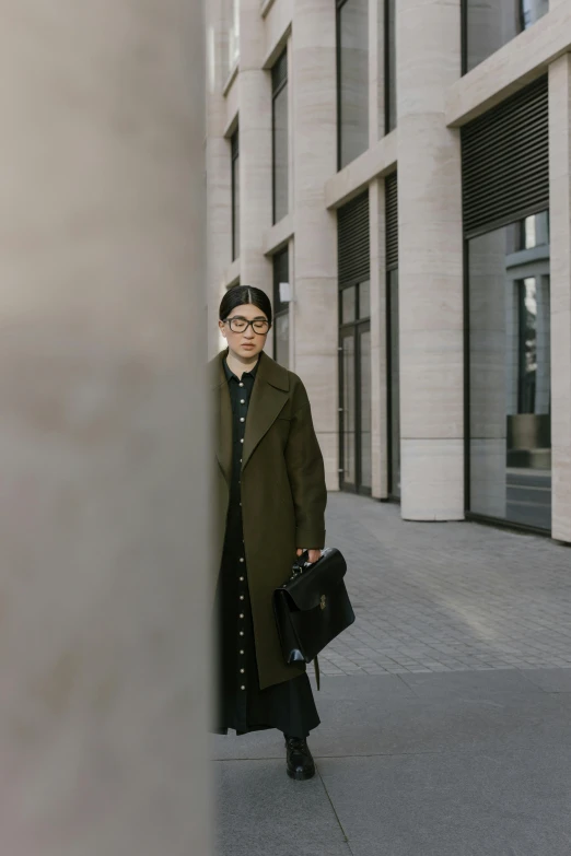 a woman in an overcoat with a suitcase on a city sidewalk