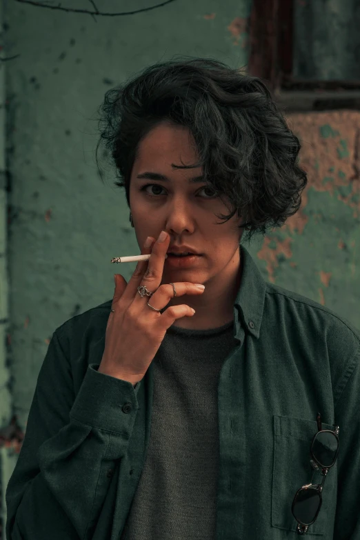 woman smoking cigarette in front of green and rusted building