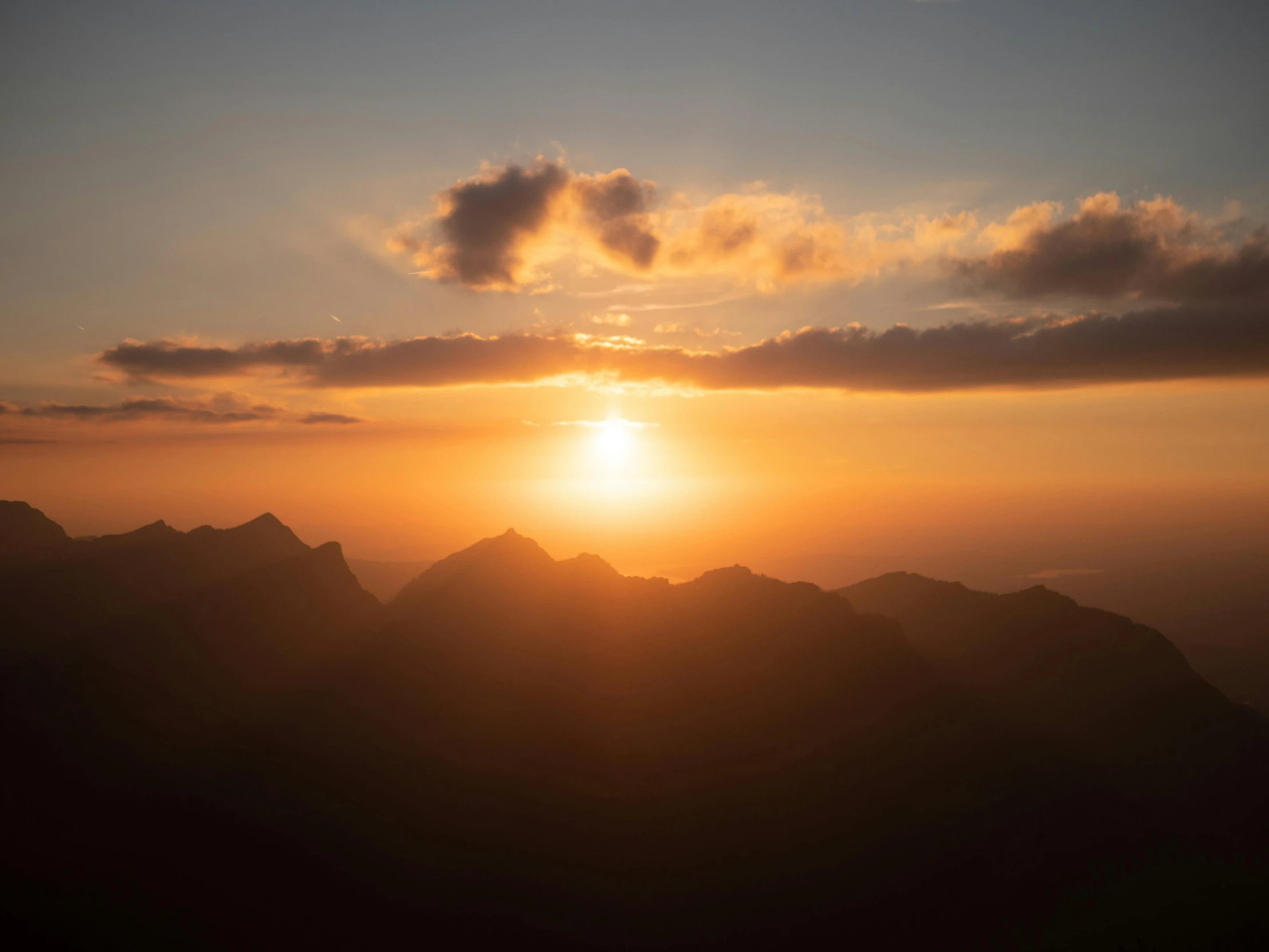 the sun is rising over some mountains with the clouds