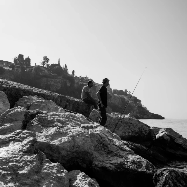 two men walking along rocks near water on a sunny day