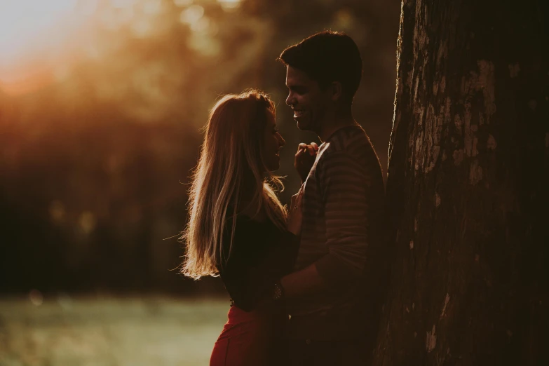 two people standing next to each other near a tree