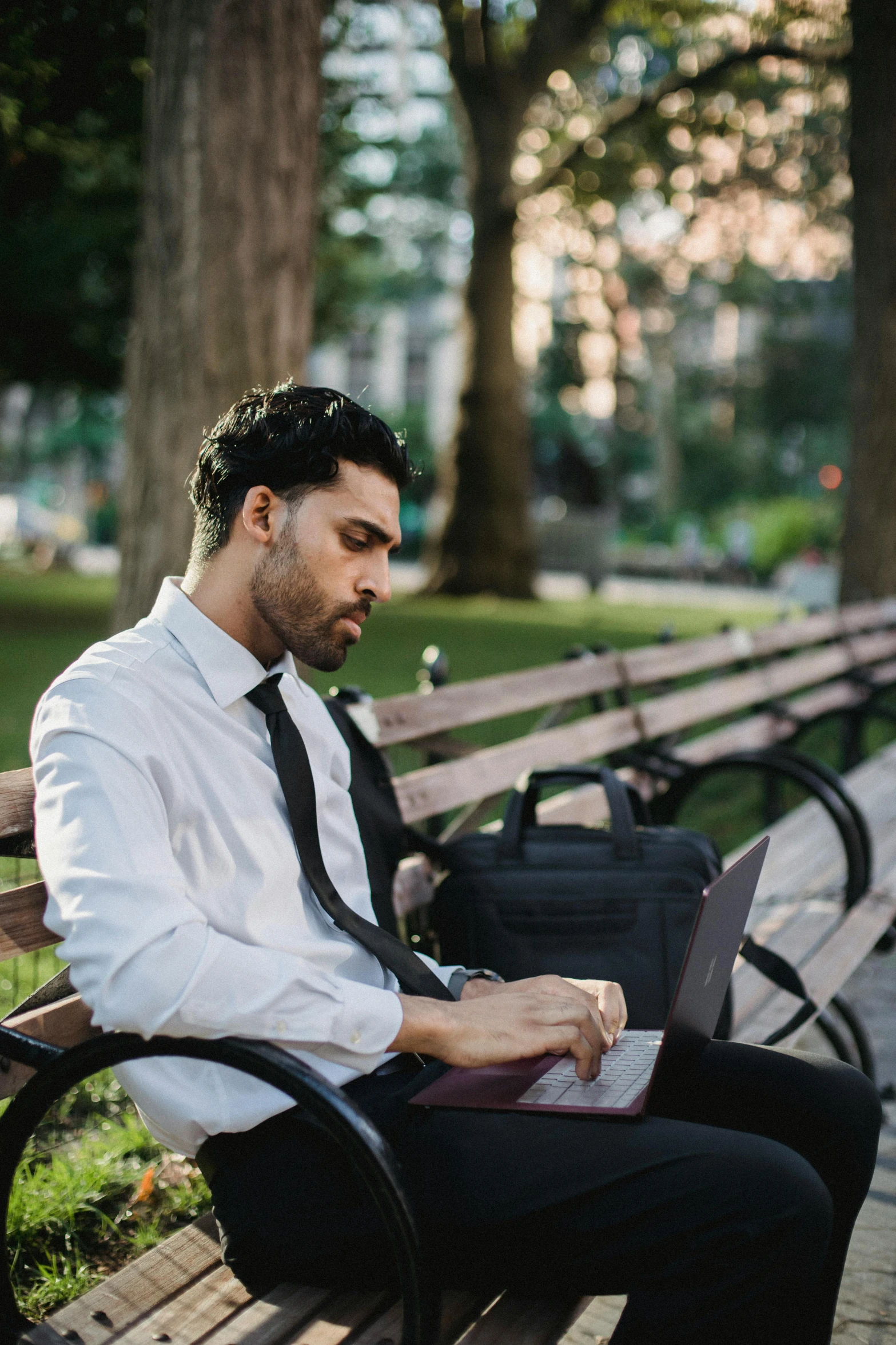 a man sits on a park bench while using his laptop