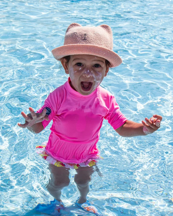 a child with a hat in water smiling and making the peace sign