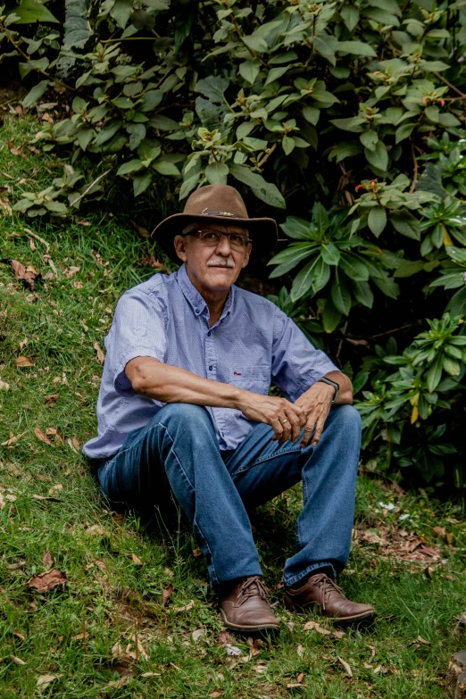 an old man wearing a hat while sitting in the grass