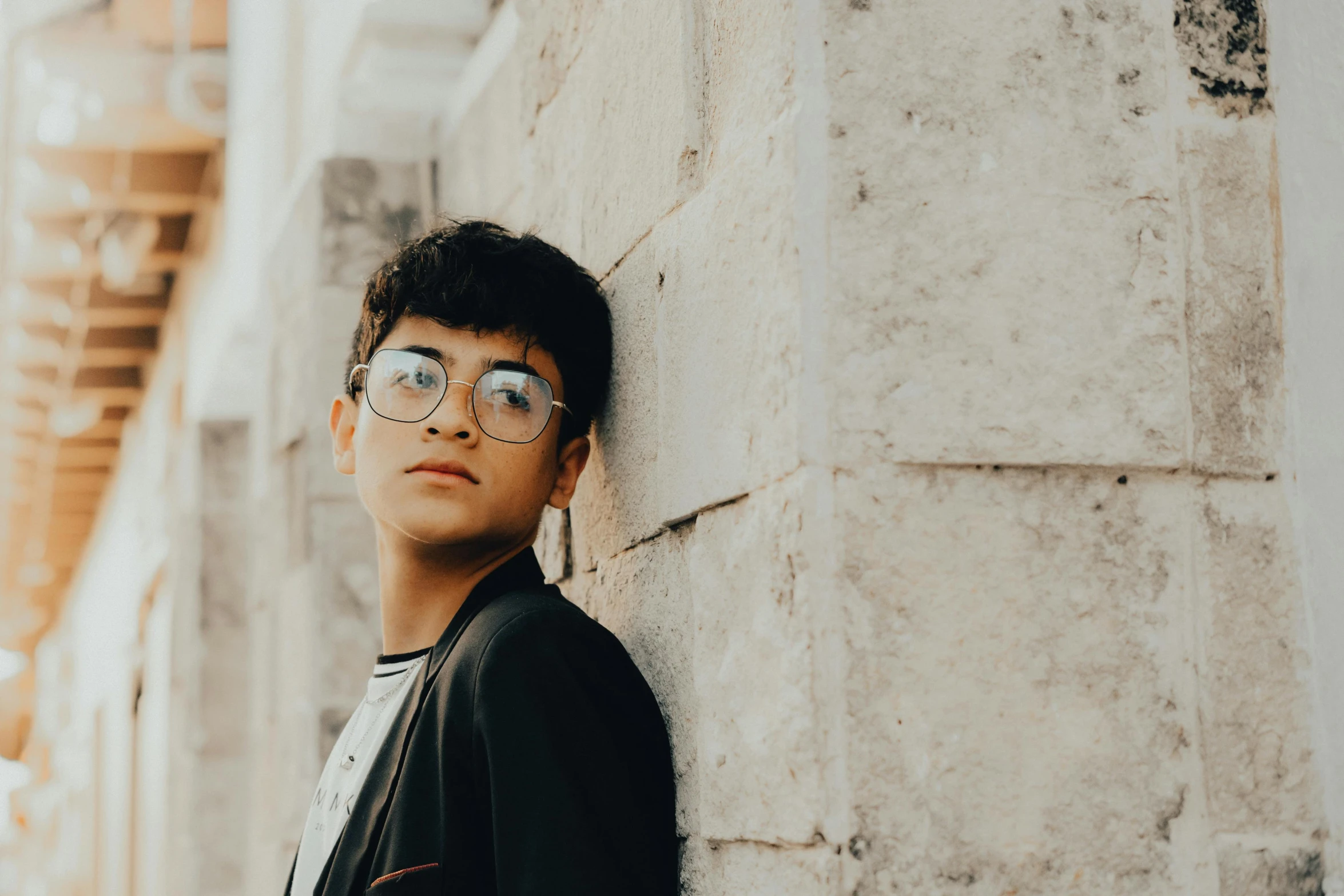 a boy with glasses leaning up against a building