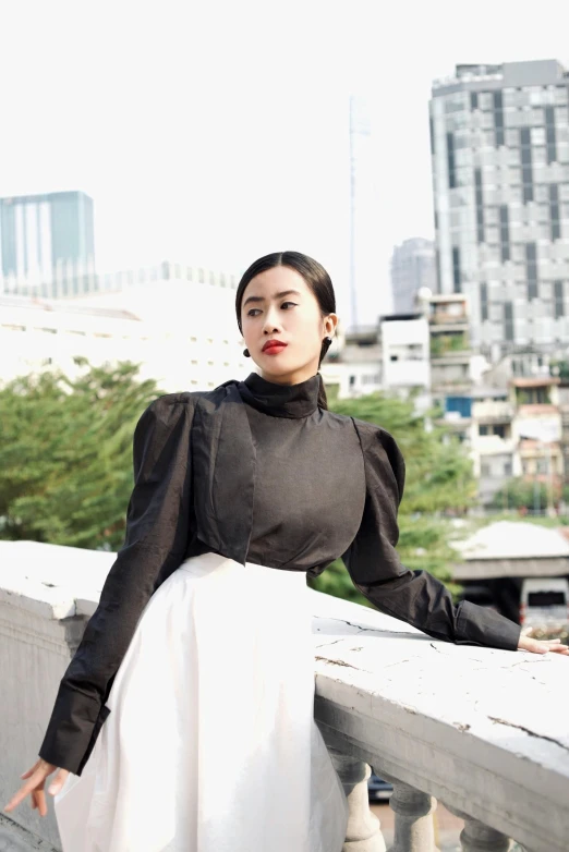 woman with a black top and skirt standing on a balcony looking off to the distance