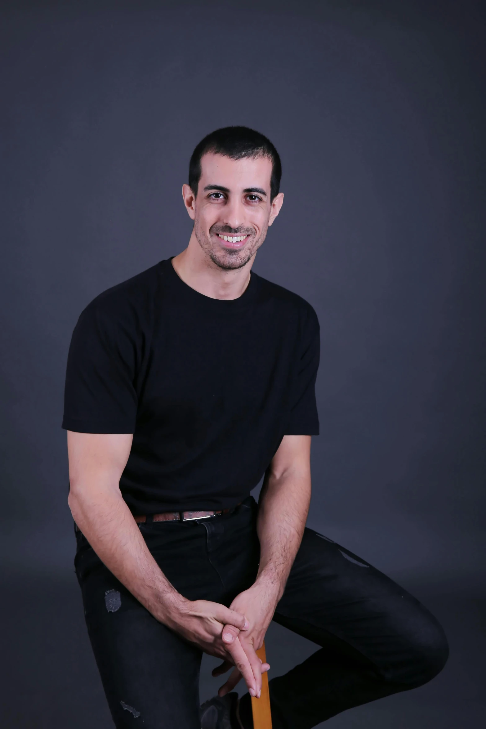 a smiling young man sitting on a stool