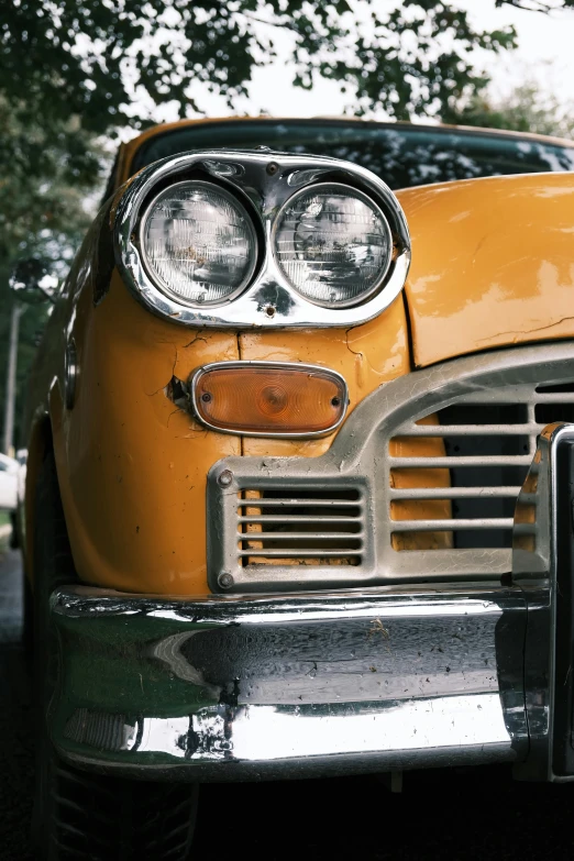 a yellow classic car on a driveway with its light on