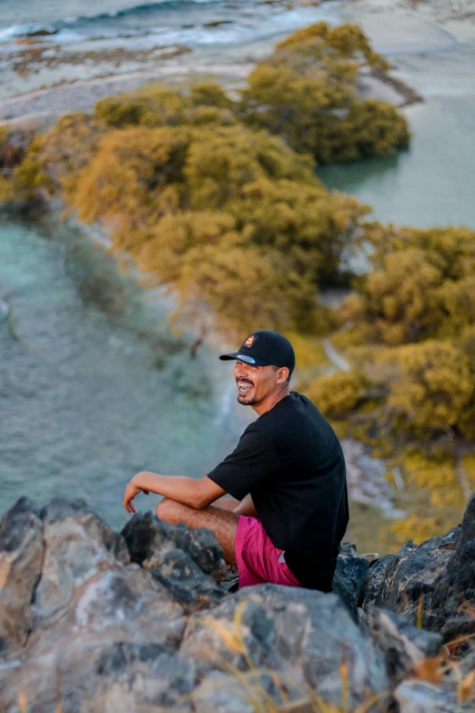 a man with a black hat and red shorts sitting on a rock