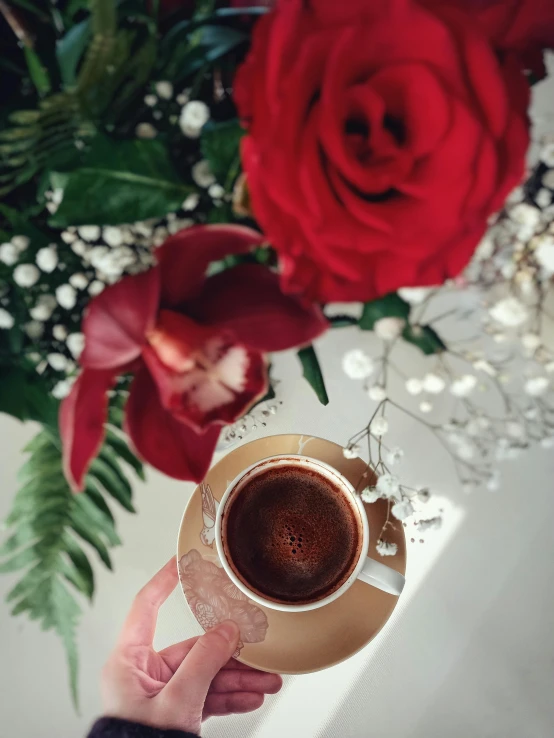 a person is holding a cup of coffee and some flowers