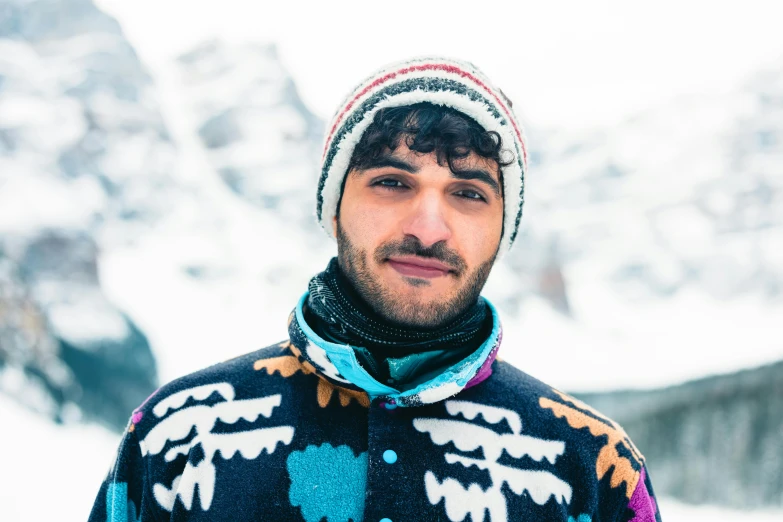 a man wearing a colorful sweater and hat standing on a mountain