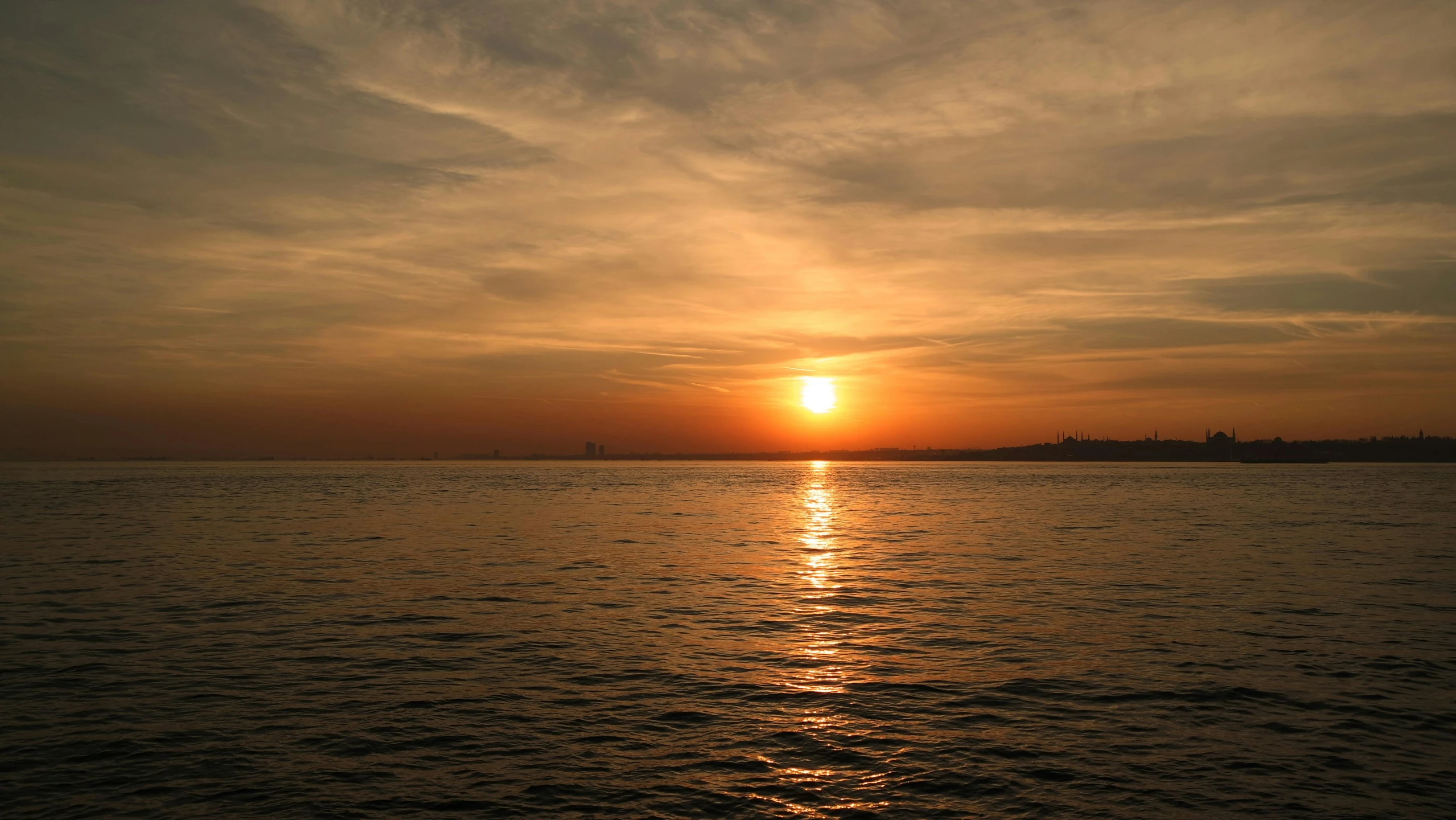 a person sitting on a surfboard with the sun setting in the distance