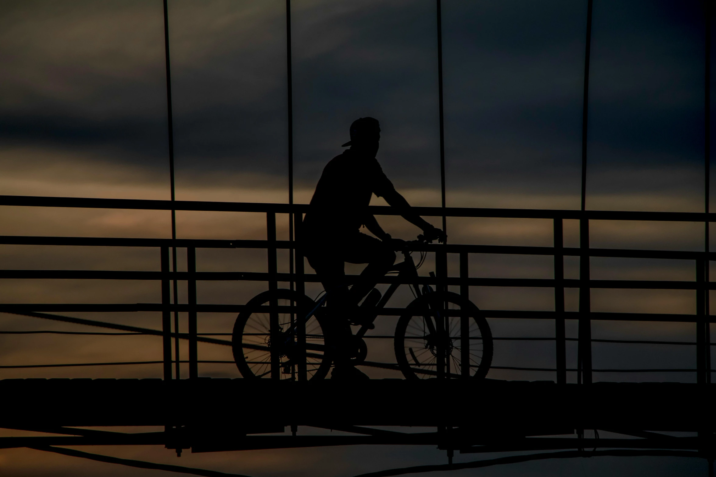 the silhouette of a person riding a bike with a cloudy sky behind