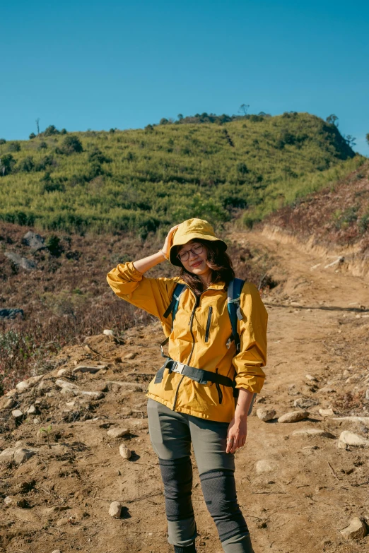 a woman standing on the side of a dirt road wearing a yellow rain coat