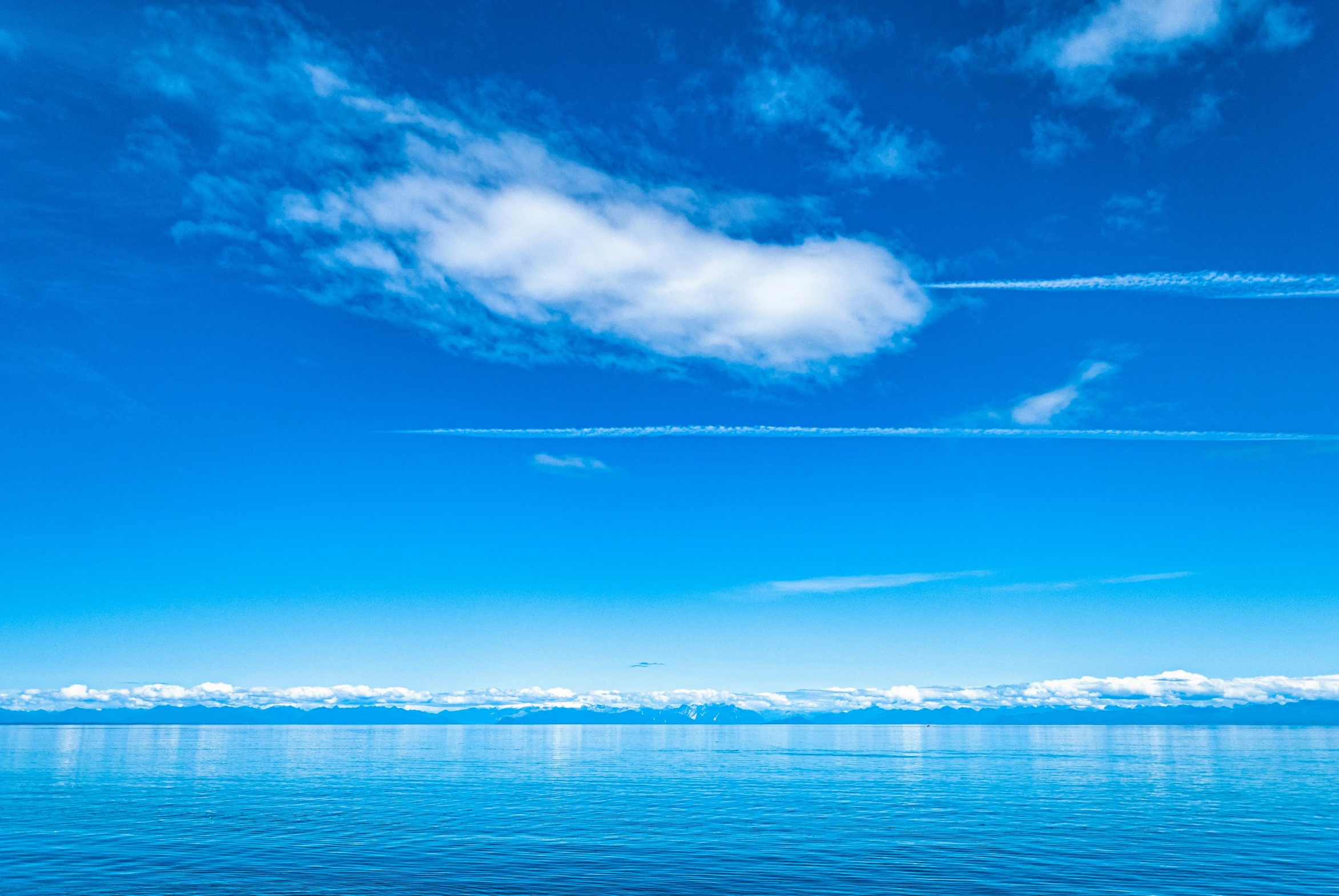 a calm body of water with contrails in the sky