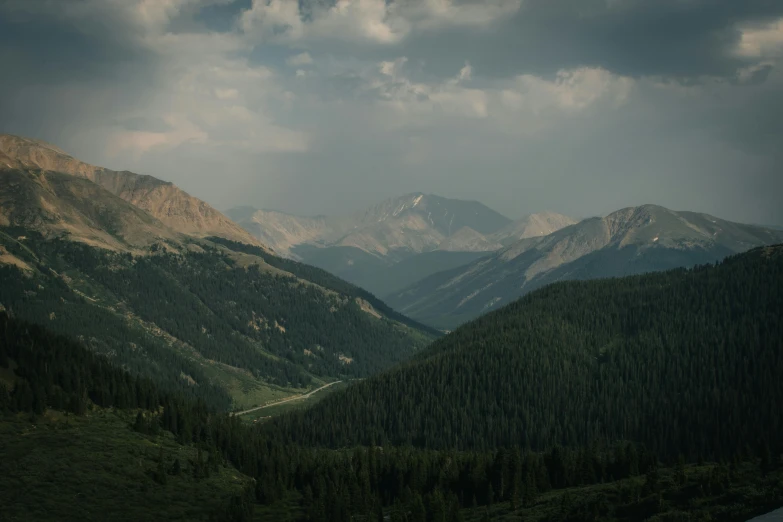 mountains, pine trees and a river under a cloudy sky