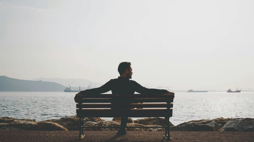 a man sitting on top of a bench next to water