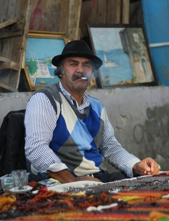 a man with hat sitting next to paintings