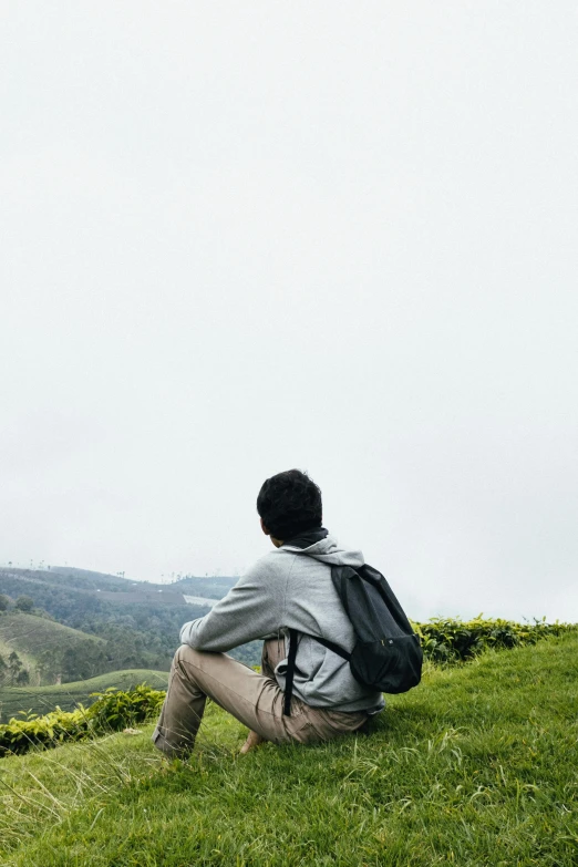 the young man is sitting on the hill looking at the view