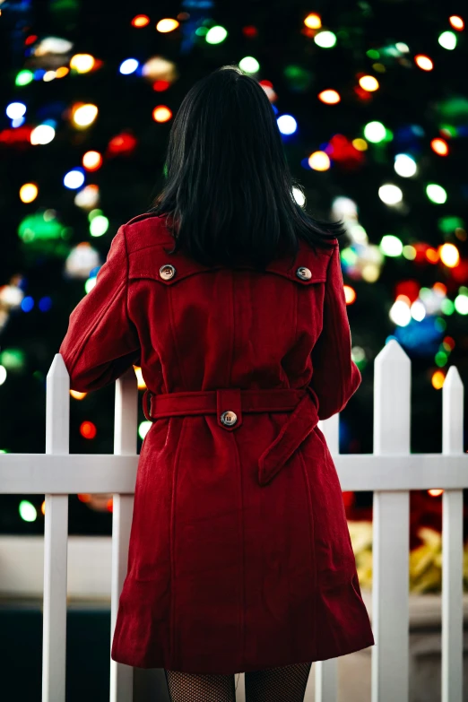 a young lady in red coat standing at a fence looking down