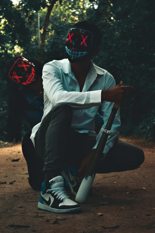 the man wearing a mask is sitting on a sidewalk holding a bat