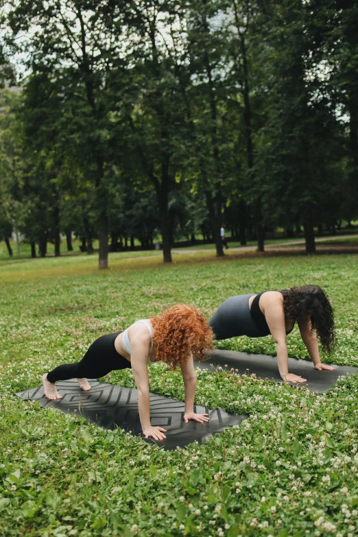 women doing yoga outdoors in park in grassy area