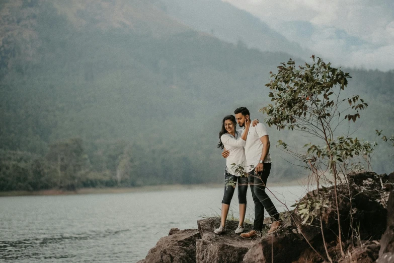 a young couple stand together on a rock overlooking a lake