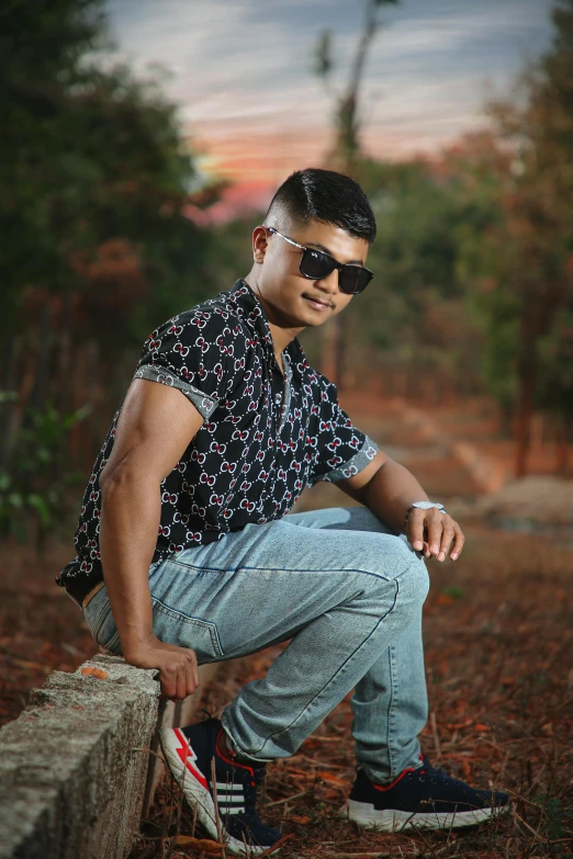 man posing with sunglasses, blue jeans and flowery shirt, leaning on a block