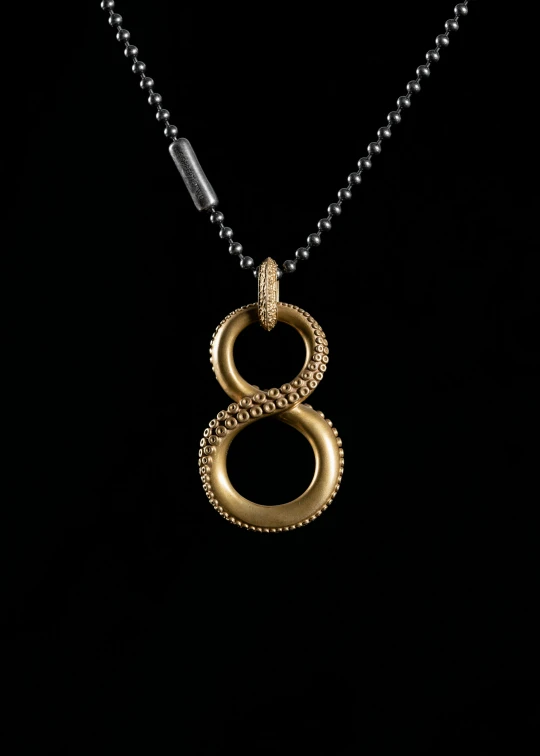 a golden serpent pendant is on display with a black necklace