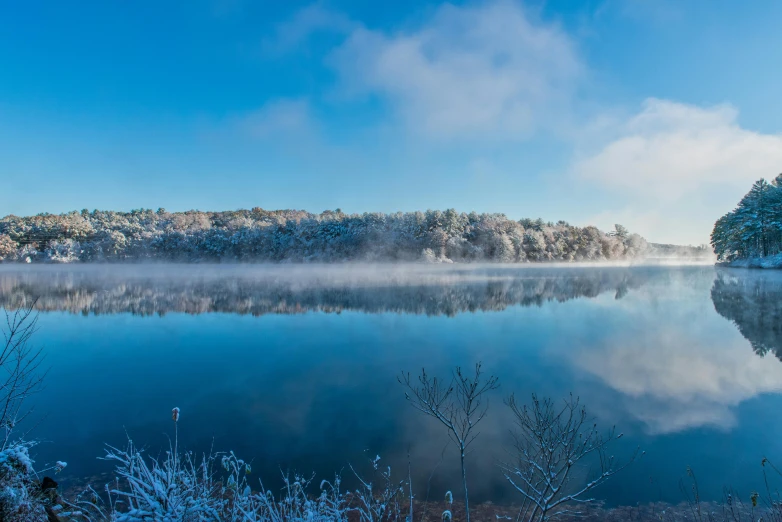 a lake surrounded by snow covered trees with fog in the middle of it