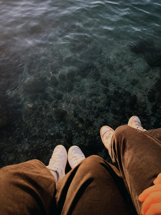 two people sitting next to each other on the rocks by the water