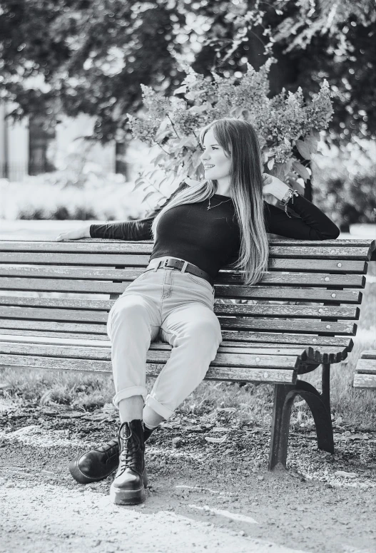 a woman sits on a park bench with her legs propped up