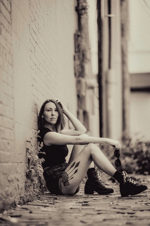 a beautiful young woman sitting on the ground leaning against a wall