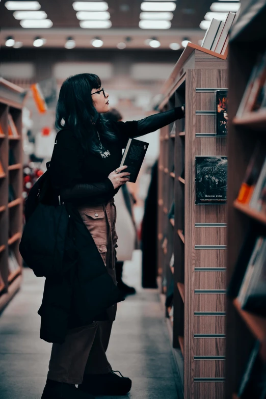 a woman with black hair standing near books in a liry