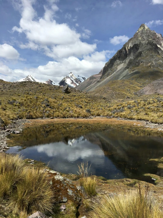 small pond on the side of a mountain with a cloudy sky