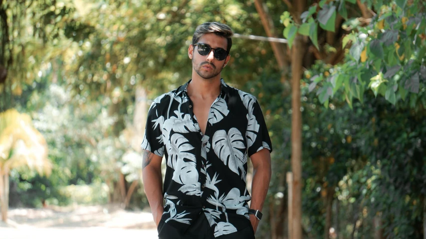 man in hawaiian shirt and sunglasses standing in the middle of a tree lined street